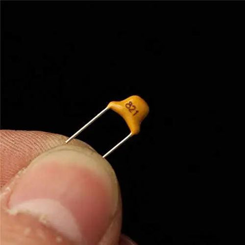 Badass 360 Piece Multilayer Ceramic Capacitors Assortment Kit 18 Values Heavy Duty NPO COG Caps 5Pf To 820Pf with visible 821 capacitor in hand.