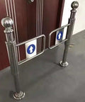 Built Solid Stainless Steel One Way Swing Gate Spring Loaded Auto Closing Security Door No Nonsense Traffic Flow For Busy Retail Shops And Industrial Warehouses, showing a polished stainless steel gate with directional arrows.