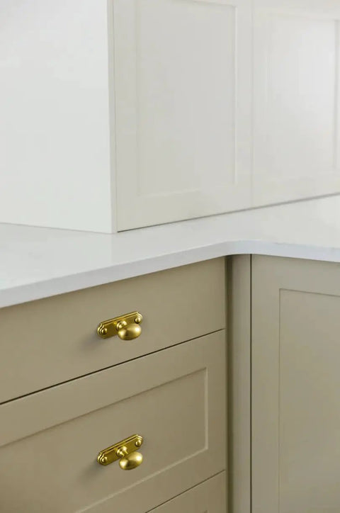 Brushed Gold Oval Cabinet Knobs Mounted On Square Backplates on drawers with beige finish, elegant design for storage solutions.