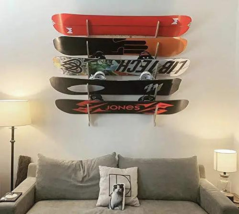 Premium Wall Rack Mount For Ski Snowboard And Longboard Storage Featuring Adjustable Baltic Birch Arms Heavy Duty Gear Holder Holds Up To One Hundred Twenty Pounds, displaying multiple snowboards on a wall above a sofa.