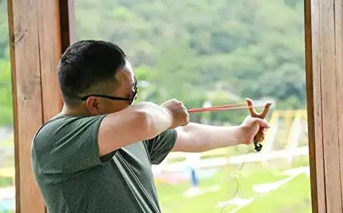 Person using a slingshot outdoors, preparing to shoot Top Tier G1000 Carbon Steel Round Balls Hefty Bulk Haul Of Five Thousand Quarter Inch Precision Metal Shot.