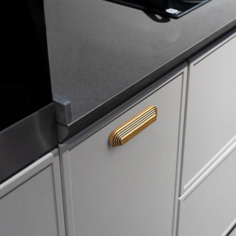 Close-up of installed Six Pack 5 Inch Antique Brass Cup Pulls With Distinctive Layered Ribbed Multi Sectioned Design on kitchen drawer.