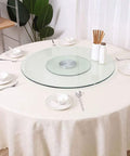 Slick Tempered Glass Lazy Susan Turntable For Kitchen Or Dining Table on a round white table with dishes and utensils.