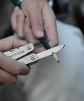 Close-up of 14 In 1 Mini Multitool Lightweight with Folding Scissors carving a pencil, showcasing its compact design and functionality.