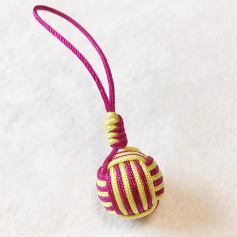 Detail of decorative pink and yellow woven ball with loop, suitable for keychain or bag accessory.