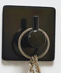 Rock Solid Black Stainless Steel Adhesive Wall Hook For Coats Towels And Umbrellas With No Hassle Peel Stick Mount Zero Drill Setup And Slick Modern Design For Bathrooms And Hallways holding keys on a wall.