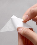 Hand holding a white adhesive shirt collar stay from a 240 Pack Invisible Adhesive Shirt Collar Stays.