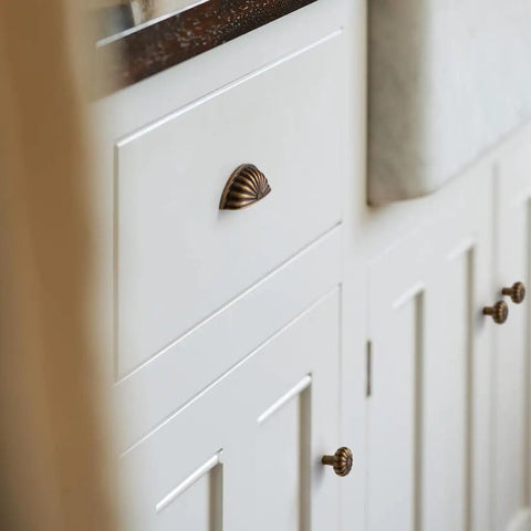 Straight Up 10 Pack Sunflower Cabinet Cup Pulls In Antique Brass Finish With Classic Retro Vibe For Kitchen Drawers And Closets featuring an antique brass half moon cup pull on a white cabinet.