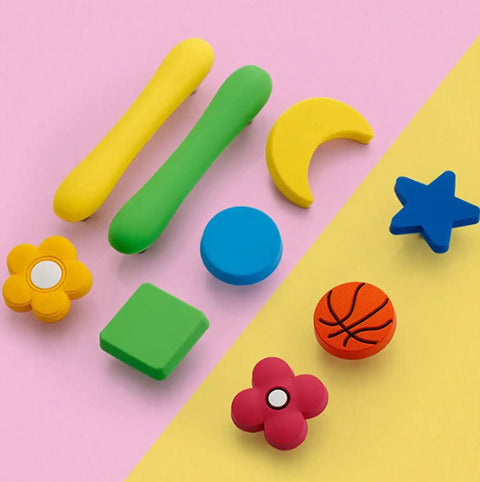 Top Shelf Cartoon Style Soft Grip Rubber Cabinet Knobs And Drawer Pulls For Kids Rooms Featuring Bulletproof Zinc Base Kid Approved Safe Finish And Zero Hassle Bolt Up Setup colorful rubber knobs in various playful shapes on pink background.
