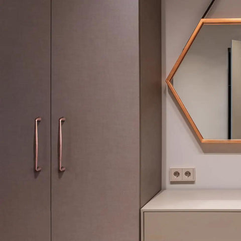 Vintage antique copper cabinet handles on sleek cabinetry with a decorative hexagonal mirror.