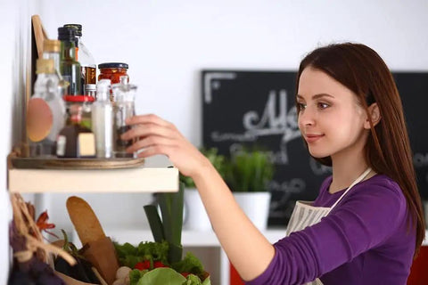 Woman organizing jars on a shelf using Smooth As Butter 14 Inch Solid Acacia Wood Lazy Susan Rotating Turntable for kitchen spices.