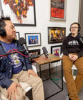 Two podcasters with closed back headphones using the Hustle Ready Podcast Creator Kit, featuring a handheld recorder and dynamic mics.