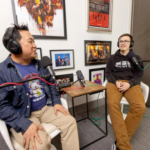 Two podcasters with closed back headphones using the Hustle Ready Podcast Creator Kit, featuring a handheld recorder and dynamic mics.