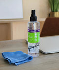 Front view of Flents Wipe 'N Clear lens cleaner spray bottle (8 oz) with blue microfiber cloth on desk.