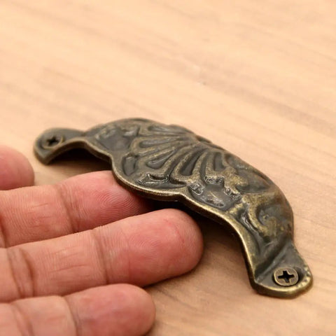 Prime Sleek Distressed Antique Brass Seashell Cabinet Pulls 8 Piece Set embossed handle shown in hand for scale on wood surface.