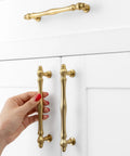 Rad Five Inch Brushed Gold Cabinet Pulls And Drawer Handles with hand installing on white cabinet doors.