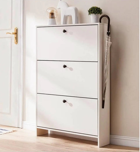 White cabinet with three drawers and black round knobs, featuring decor items on top and an umbrella hanging on the side.