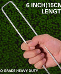 Hand holding heavy duty 6 inch garden landscape staple, U shaped, 11 gauge galvanized pin, pro grade visible on grass surface.