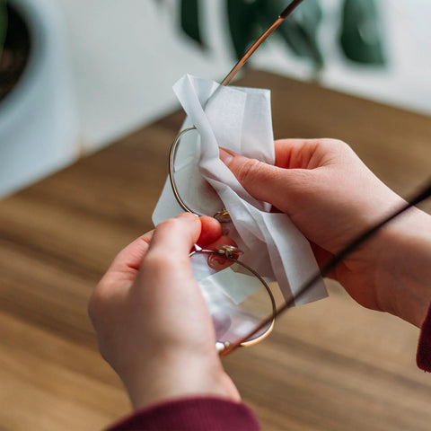 VOISEN lens wipes for eyeglasses being used on metal-frame glasses; pre-moistened wipe.