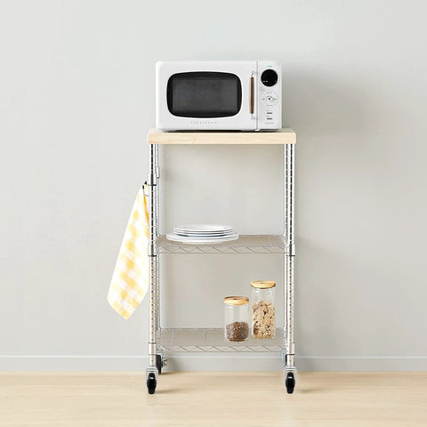 Metal wire kitchen cart with microwave, plates, and jars, on wheels, against a white wall.