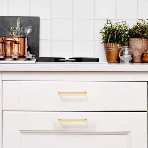 10 Pack Brushed Gold Cabinet Handles And Drawer Pulls For Kitchen Cabinets And Dressers Featuring Slick Zinc Alloy Body With Dope Fresh Look Plus 3.75 Inch Hole Spacing Great For Snazzy Vibe Upgrade Of Drawers And Cupboards Today displayed on white drawers in a modern kitchen.