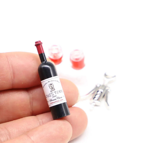 Hella Cool Miniature Red Wine Bottle Set Featuring two resin filled wine glasses and a static corkscrew for dollhouse decor, showing a hand holding a 38 mm wine bottle.