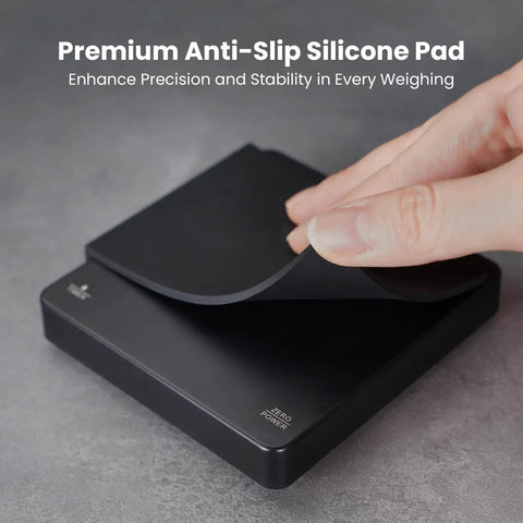 Close-up of palm sized coffee scale with timer for espresso and pour over brews rechargeable digital kitchen scale with 2 kg capacity and 0.1 gram increments portable black pro level precision for home baristas, featuring anti-slip silicone pad.