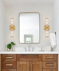 Bathroom view with Gold Wall Sconce Lights Two Pack With Candle Shaped Glass Shades flanking a mirror on wooden vanity.