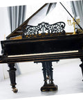 Antique black grand piano with ornate lid, featuring elegant legs and wheels for easy mobility in a bright room.
