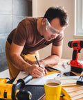 Man wearing Real Deal 6 Pack Clear Lab Safety Glasses Featuring Ventilated Side Shields And Lightweight Wraparound Design, writing on a desk.