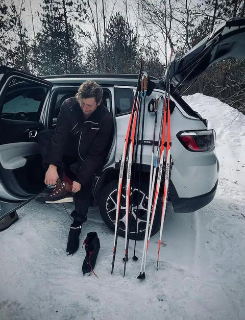 Badass Magnetic Ski And Snowboard Vehicle Rack Keeping Your Ride Spotless With Soft Waterproof Padding For Reliable All Season Winter Storage And Trail Ready Adventures. Man fastening boots near vehicle with skis ready.