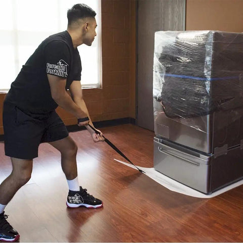 Man using giant appliance slider with pull strap to move heavy washer while protecting floors from scratches.