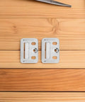 Two stainless steel snap lock mounting clips on wooden surface, part of 100 Piece Stainless Steel Wall Panel Buckles Hardcore Snap Lock Mounting Clips Zero Hassle Quick Setup For Drywall Furring Strips Baseboards Furniture Fixes Rock Solid Hold For Home Office Spaces.