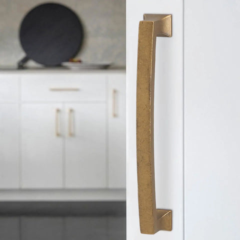 Hella Durable Five Inch Antique Brass Cabinet Pulls And Drawer Handles With Smooth Satin Finish on a white cabinet door.