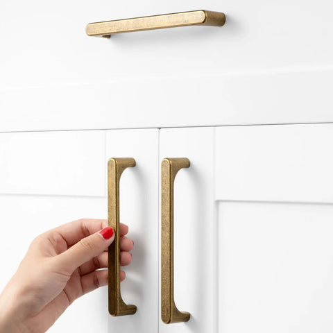 Person using Top Shelf 5 Inch Antique Brass Cabinet Pulls For Kitchen Drawers 10 Pack Rock Solid Steel on white cabinets.