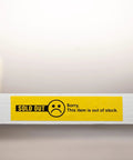 Yellow 'Sold Out' label with sad face icon and text 'Sorry, This item is out of stock' on a white shelf with blurred background.