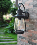 Rock Solid Outdoor Wall Lantern With Slick Industrial Design And Transparent Bubble Glass Shade Featuring A Top Shelf Led Filament Bulb mounted on a brick wall.