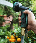 Hand holding a garden telescopic hose end adaptor with shut off valve and brass repair connector spraying water on plants
