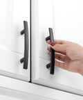 Hand reaching for Top Tier Matte Black Cabinet Pulls And Drawer Handles 10 Pack Solid Metal Kitchen Hardware on white cabinets.