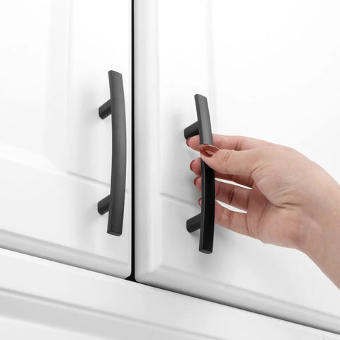 Hand reaching for Top Tier Matte Black Cabinet Pulls And Drawer Handles 10 Pack Solid Metal Kitchen Hardware on white cabinets.