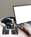 Hella Sturdy Under Desk Laptop Holder Two Pack With Reinforced Steel Frame And Antislip Eva Base on a desk next to a laptop and headphones.