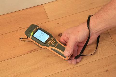 SurveyMaster Dual Function Moisture Meter With Pin And Non Invasive Modes in use on wood floor displaying 14.5 reading