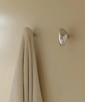 Sweet Looking Pebble Wall Hook Built From Top Shelf 304 Stainless Steel holding a towel on a light beige wall.