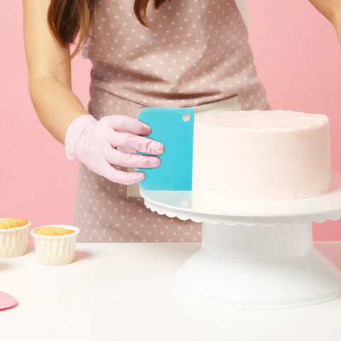 Next Level Cake Decorating Kit Featuring Hella Durable Anti Burst Piping Bags Stainless Steel Frosting Tips Set And Reusable Pastry Supplies For Baking Like A Champ Zero Worries, featuring a cake being smoothed with a blue scraper.