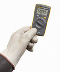Gloved hand holding Compact Digital Multimeter With 6000 Count Display And 600V AC And DC Range And Accurate Voltage And Resistance Readouts