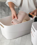 Top Shelf White Plastic Storage Basket With Lidless Opening For Zero Fuss Organization And Straight Up Space Saving Efficiency Ideal For Cozy Living Room Or Bedroom Vibes, holding a rolled towel.