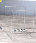 Must Have Pendulum Frame Physics Desk Toy For Learning And Decor, Cradle Style Science Education Gadget in silver on wooden surface
