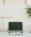 West 15 Inch LED Integrated Desk Lamp in matte brass on modern workspace with laptop and plant.