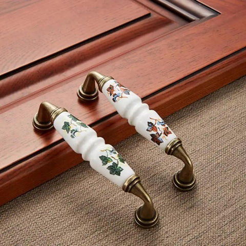 10 Pack Vintage Ceramic Cabinet Pulls Featuring Hella Charming Red Floral Motifs On Creamy White Porcelain Base Coupled With Antique Bronze Zinc Alloy Hardware For Authentic French Country Kitchen Cabinets Drawers And Furniture 96mm Hole Centers, displayed on wood.