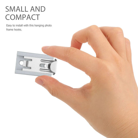 Hand holding a small, silver heavy duty stainless steel picture hanger for easy installation, part of a four pack.
